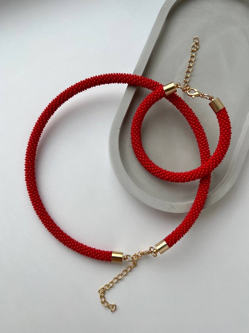 Pu&ograve; includere: Un set di collana e braccialetto di perline rosse con chiusure dorate. La collana &egrave; pi&ugrave; lunga del braccialetto.