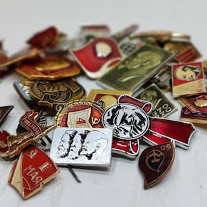 Può includere: Una collezione di spille smaltate vintage con vari disegni, tra cui ritratti, bandiere e simboli. Le spille sono principalmente rosse, bianche e blu, con alcuni accenti dorati.