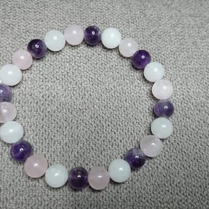 May include: A bracelet made of white, pink, and purple beads. The beads are round and smooth.