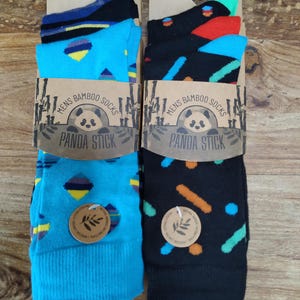 May include: Three pairs of bamboo socks in a colourful geometric pattern. The socks are packaged in a cardboard box with a panda logo and the text "Mens Bamboo Socks Panda Stick".