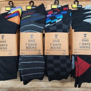 Könnte beinhalten: Vier Sets Cotton King 7 Days Socken, jeweils mit sieben Paaren. Die Packungen zeigen verschiedene Muster, darunter einfarbiges Schwarz mit farbigen Fersen, horizontale Streifen, Karomuster und rote Rautenmuster, alle mit der Kennzeichnung UK 6-11.