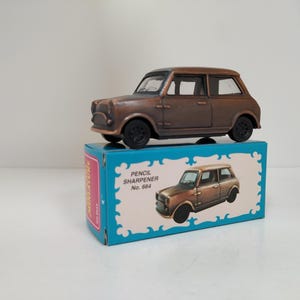 Könnte beinhalten: Ein brauner Bleistiftspitzer aus Metall in Form eines klassischen Mini Cooper. Der Spitzer befindet sich in einer blauen Schachtel mit dem Text "Pencil Sharpener No. 664".