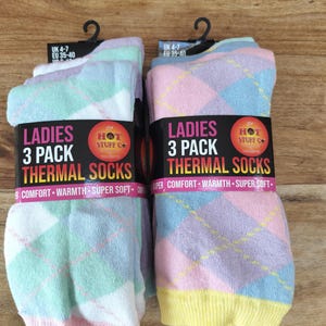 May include: Two packs of three thermal socks featuring a pastel argyle pattern in shades of pink, blue, green, and yellow. Each pack includes a black label with the text LADIES 3 PACK THERMAL SOCKS, COMFORT, WARMTH, SUPER SOFT, and HOT STUFF CO.