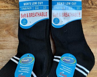 以下が含まれることがあります： 白のストライプとタグが付いた、黒のローカットソックスが2足。タグには「MEN'S LOW CUT」と「Soft & BREATHABLE」と書かれています。各靴下には「Fresh」タグがあり、吸汗性と耐摩耗性を宣伝しています。
