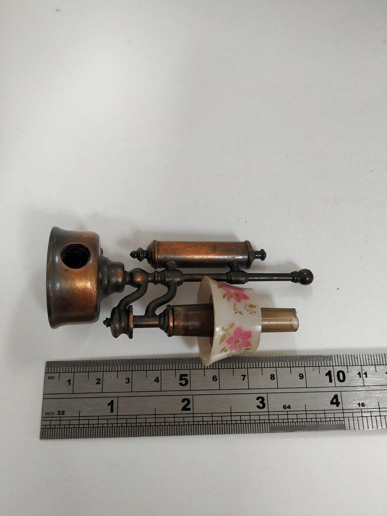 May include: An antique brass and copper-toned lamp with a floral patterned lampshade. The lamp is approximately 4 inches long and features a detailed design. A ruler is placed next to the lamp for scale.