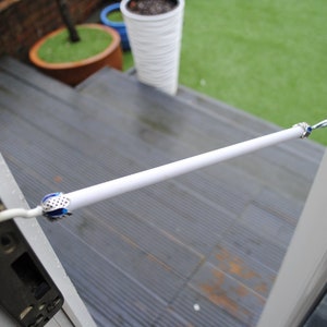 May include: A white door security bar with blue and silver accents. The bar is attached to the door with a metal hook and a chain. The bar is extended across the door to prevent it from opening.