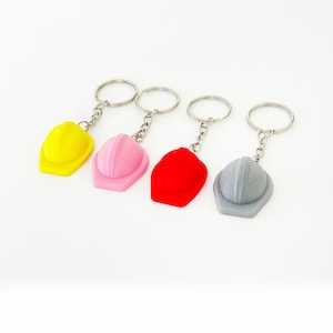 May include: Four keychains with different colored hard hats. The hats are yellow, pink, red, and gray.