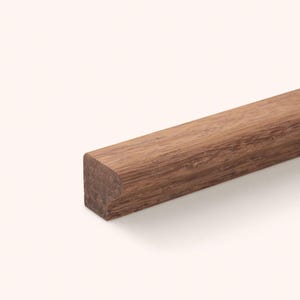 Può includere: Un segmento dritto di modanatura in legno massello caratterizzato da una tonalità marrone medio con una venatura naturale visibile. L'elemento presenta un profilo rettangolare con un bordo arrotondato e una superficie liscia e rifinita.