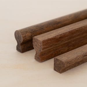 May include: Three wooden drawer pulls with a rounded, slightly curved design. The pulls are a dark brown color and have a natural wood grain.
