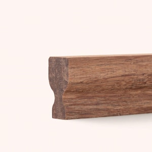 May include: A straight length of brown wooden molding with a distinct profile featuring a concave groove along the side. The wood displays a natural grain pattern with varying shades of brown, showcasing a smooth, finished surface texture.