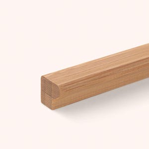 Può includere: Un lungo pezzo dritto di modanatura in bambù marrone chiaro con una sezione trasversale rettangolare caratterizzata da un bordo arrotondato su un lato. La venatura del legno è visibile lungo il pezzo, mostrando la trama e le fibre naturali.