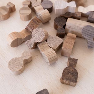 May include: A collection of small, wooden, abstract shapes in various shades of brown and tan. The shapes include rounded, bottle-like forms, rectangular blocks, and other geometric designs. The pieces are scattered on a light wood surface.
