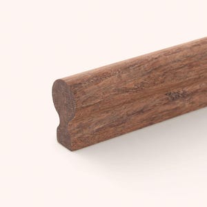 Può includere: Una sezione di corrimano in legno marrone scuro caratterizzata da un profilo superiore liscio e arrotondato che si restringe verso una base più sottile. La venatura del legno è visibile su tutta la superficie, mostrando texture naturali e toni.