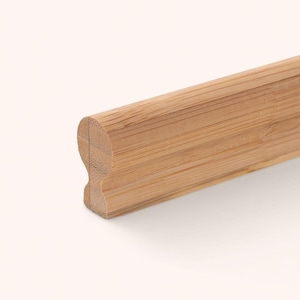 May include: A long, straight piece of light brown bamboo moulding with a distinct profile. The cross-section shows a rounded top edge that curves inward to a narrower neck, creating a decorative shape with a visible natural wood grain texture.