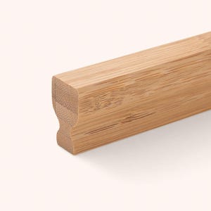Può includere: Una striscia di legno di bambù marrone chiaro caratterizzata da un distinto motivo a venature longitudinali e da un profilo laterale sagomato con un'indentazione concava che corre lungo la lunghezza del pezzo, evidenziando la fibra naturale.