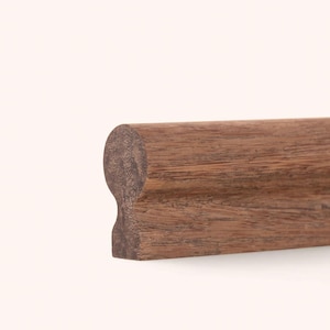 May include: A length of brown wooden molding with a rounded top profile and a recessed groove along the side. The wood grain is visible throughout the surface, showing a natural texture and medium brown color in this horizontal orientation.