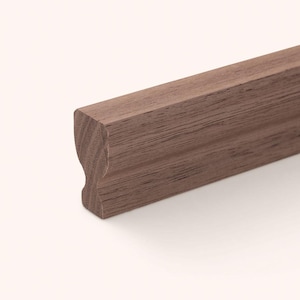 Può includere: Una lunghezza di modanatura in legno marrone scuro con un profilo distinto caratterizzato da un'indentazione curva su un lato e un bordo superiore piatto. La venatura del legno è visibile su tutta la superficie, mostrando motivi lineari.
