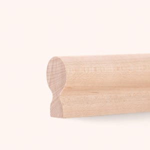 Peut inclure: Une main courante en bois clair présentant un profil supérieur lisse et arrondi qui se transforme en un col concave et une base plus large et plate. Le grain du bois est visible sur la surface, montrant une texture beige clair naturelle.