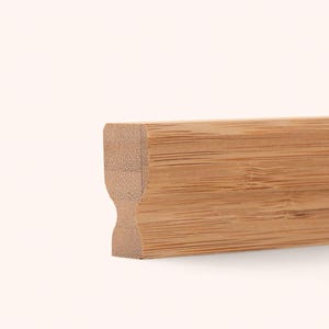 May include: A rectangular piece of light brown bamboo wood with a distinct horizontal grain pattern. The left side features a concave, hourglass-shaped profile, while the remaining length maintains a straight, uniform edge along the top and bottom.