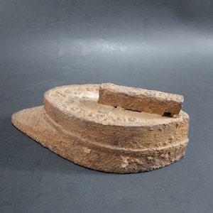 May include: A vintage cast iron flat iron with a raised handle. The iron is rusty and has a worn surface.