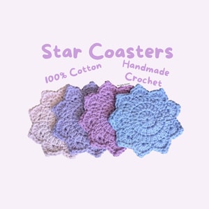 May include: Five handmade crochet star coasters in shades of lavender, purple, and blue. The coasters are made of 100% cotton and are arranged on a light pink background. Text on the image reads "Star Coasters, 100% Cotton, Handmade Crochet."