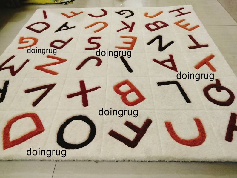 K&ouml;nnte beinhalten: Wei&szlig;er Teppich mit braunen, roten und schwarzen Buchstaben, die darauf gestickt sind. Die Buchstaben sind in zuf&auml;lliger Reihenfolge angeordnet und buchstabieren mehrmals das Wort "doingrug".