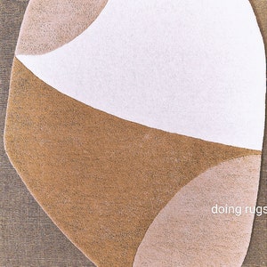K&ouml;nnte beinhalten: Ein abstrakter Teppich mit einer einzigartigen Form, der wei&szlig;e, beige und braune Bereiche aufweist. Das Design ist geometrisch, mit geschwungenen Linien und einer weichen Textur. Geeignet f&uuml;r Wohn- oder Schlafzimmer. Ma&szlig;e in Zentimetern.