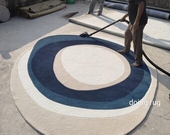 May include: A round rug with concentric oval patterns in shades of beige, white, navy blue, and light blue. The rug is being cleaned with a vacuum cleaner. The text "doing rug" is visible on the rug.