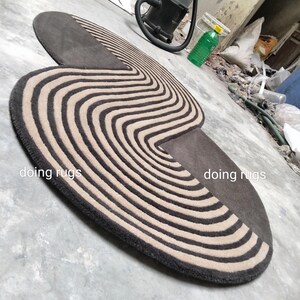 May include: A brown and beige striped rug with a unique curved shape. The rug has a modern design and is perfect for adding a touch of style to any room. The rug is made of high-quality materials and is durable enough for everyday use. "doing rugs" is written on the rug.
