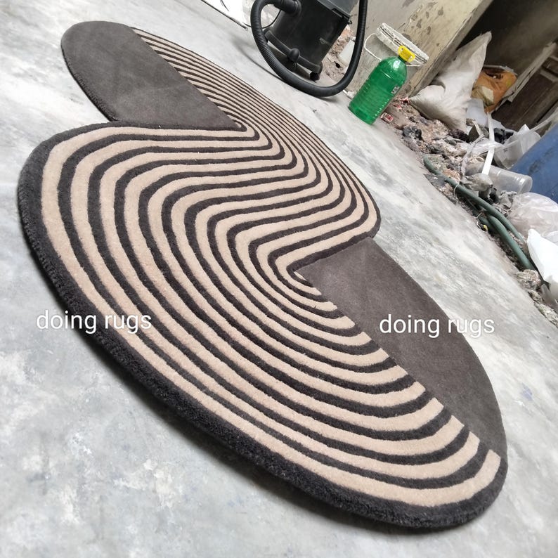 May include: A brown and beige striped rug with a unique curved shape. The rug has a modern design and is perfect for adding a touch of style to any room. The rug is made of high-quality materials and is durable enough for everyday use. "doing rugs" is written on the rug.
