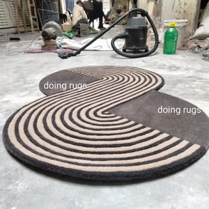 May include: A brown and beige striped rug with a unique, curved shape. The rug is made of wool and has a soft, plush texture. The text "doing rugs" is written on the rug.