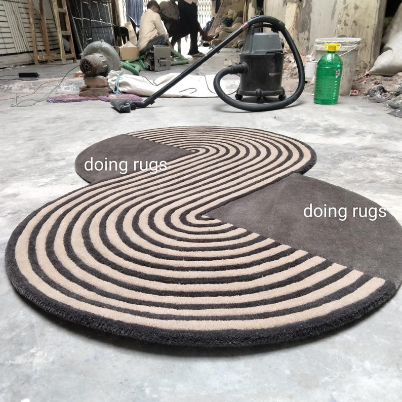 May include: A brown and beige striped rug with a unique, curved shape. The rug is made of wool and has a soft, plush texture. The text "doing rugs" is written on the rug.
