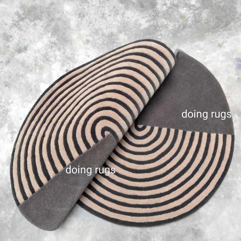 May include: A round, brown and beige rug with a spiral pattern. The rug is folded in half, revealing the back side, which is a solid brown color. The text "doing rugs" is visible on the rug.
