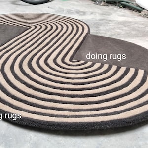 May include: A large, brown and cream striped rug with a unique, curved shape. The rug has a modern design and is perfect for adding a touch of style to any room. The text "doing rugs" is visible in the image.