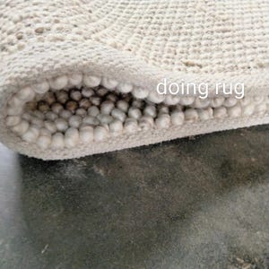May include: Close-up of a rolled-up, off-white rug with a textured, nubby surface. The rug's edge reveals a dense, rounded interior. The text "doing rug" is visible on the rug's surface.