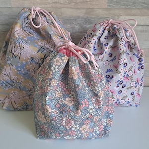 Könnte beinhalten: Drei Beutel mit Kordelzug und Blumenmustern in Blau-, Rosa- und Grautönen. Die Beutel haben rosa Kordelzüge und sind auf einer weißen Oberfläche vor einem neutralen Hintergrund angeordnet. Die Beutel sind unterschiedlich groß.
