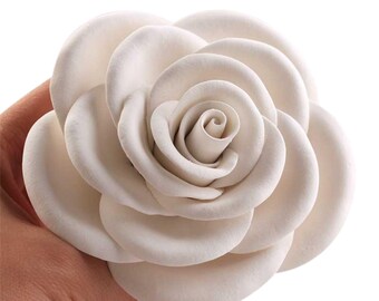 Puede incluir: Una rosa de cerámica blanca con múltiples capas de pétalos. La rosa es un adorno decorativo para el hogar.