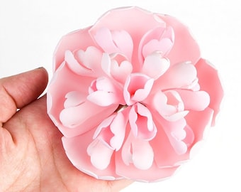 May include: A pink fabric flower with a layered, ruffled design. The flower is made of multiple petals that are arranged in a circular pattern.