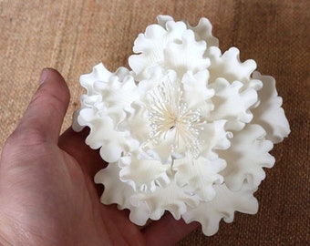 May include: A white sugar flower resembling a peony with ruffled petals.