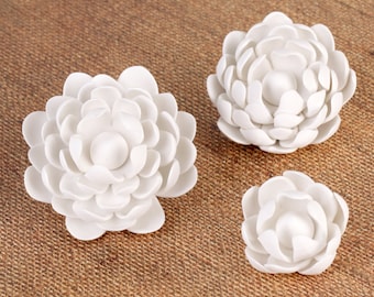 May include: Three white ceramic flower decorations. The flowers are made of many small petals and have a simple, elegant design.