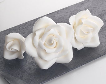 May include: Three white sugar roses on a gray background. The roses are different sizes and are arranged in a row.