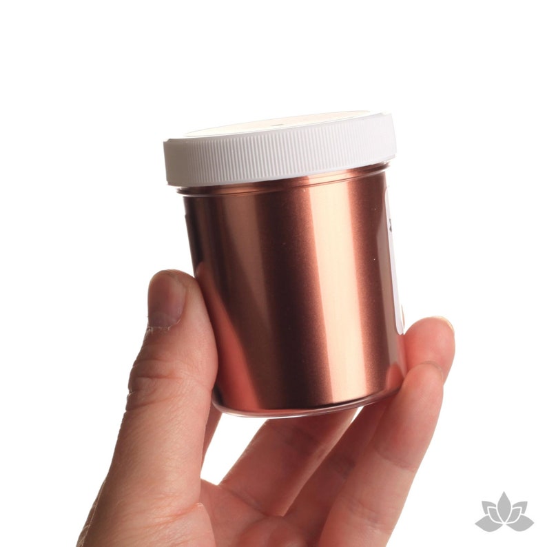 May include: A small jar of copper mica powder with a white lid. The jar is being held in a hand.