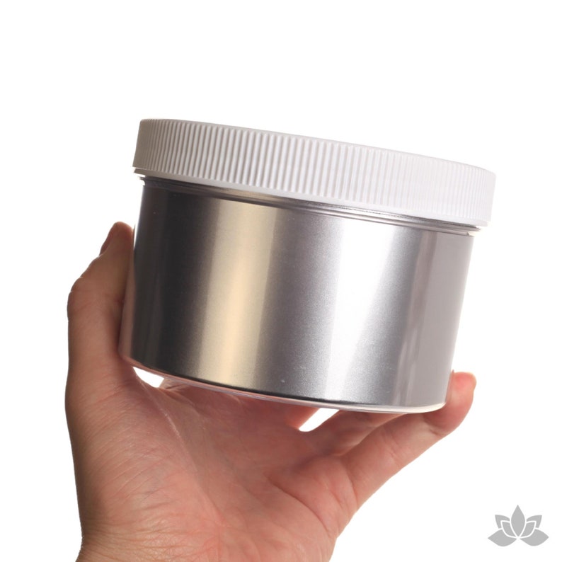 May include: A silver metallic paint in a white plastic jar with a white lid. The jar is being held in a hand.