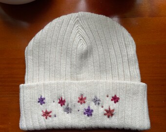 Puede incluir: Gorro de punto blanco con textura de canalé y flores bordadas en tonos rosa, morado y rojo.