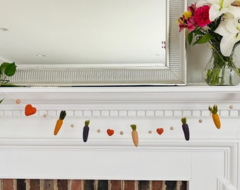 May include: A felt garland with carrots and hearts, hanging above a white fireplace mantel.