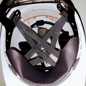 May include: White hard hat with a black padded interior and a black suspension system. The suspension system has a criss-cross pattern and is adjustable. The hard hat has a label with safety information.