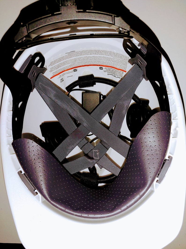 May include: White hard hat with a black padded interior and a black suspension system. The suspension system has a criss-cross pattern and is adjustable. The hard hat has a label with safety information.