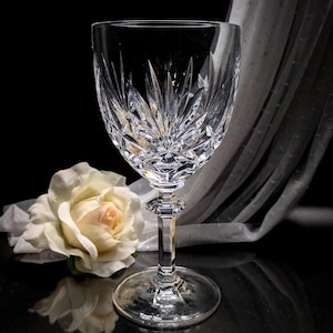 May include: A clear crystal wine glass with a cut design. The glass has a tall stem and a round base.