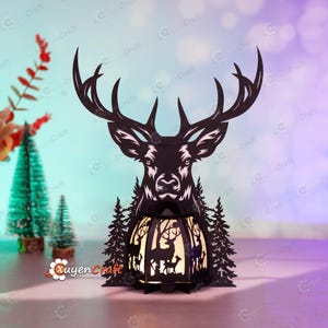 May include: A black silhouette of a deer head with antlers, with a small, illuminated, wooden lamp in the shape of a forest scene. The lamp has a white light and features a deer, trees, and other forest elements.