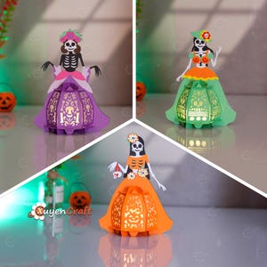 May include: Three paper lanterns shaped like skeleton figures, each with a different coloured dress. The lanterns are purple, green, and orange, and have intricate cut-out designs. The lanterns are decorated with floral crowns and are lit from within.
